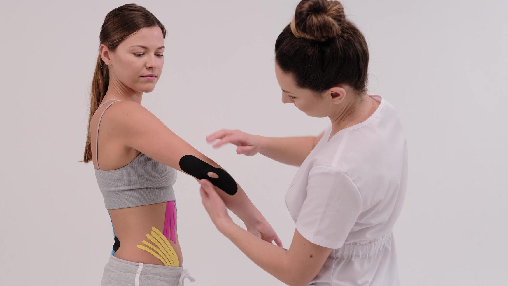 una fisioterapeuta mide un trozo de kinesiotape para aplicarlo en la articulación del hombro. dobla una mano en el codo para comprobar foto