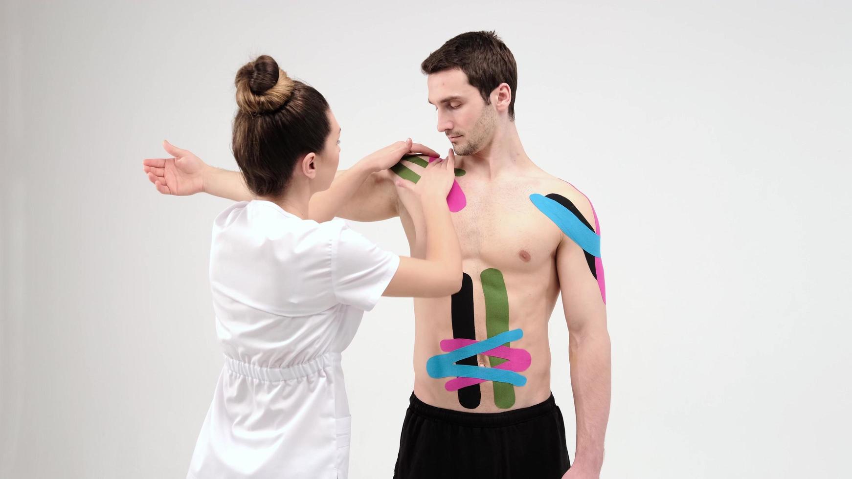 tratamiento de hombros con kinesio tape. Fisioterapeuta aplicando cinta terapéutica elástica a la lesión del hombro del paciente foto
