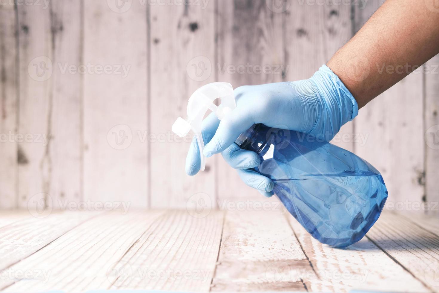 Mano en guantes de goma azul sosteniendo la mesa de limpieza de botellas de spray foto