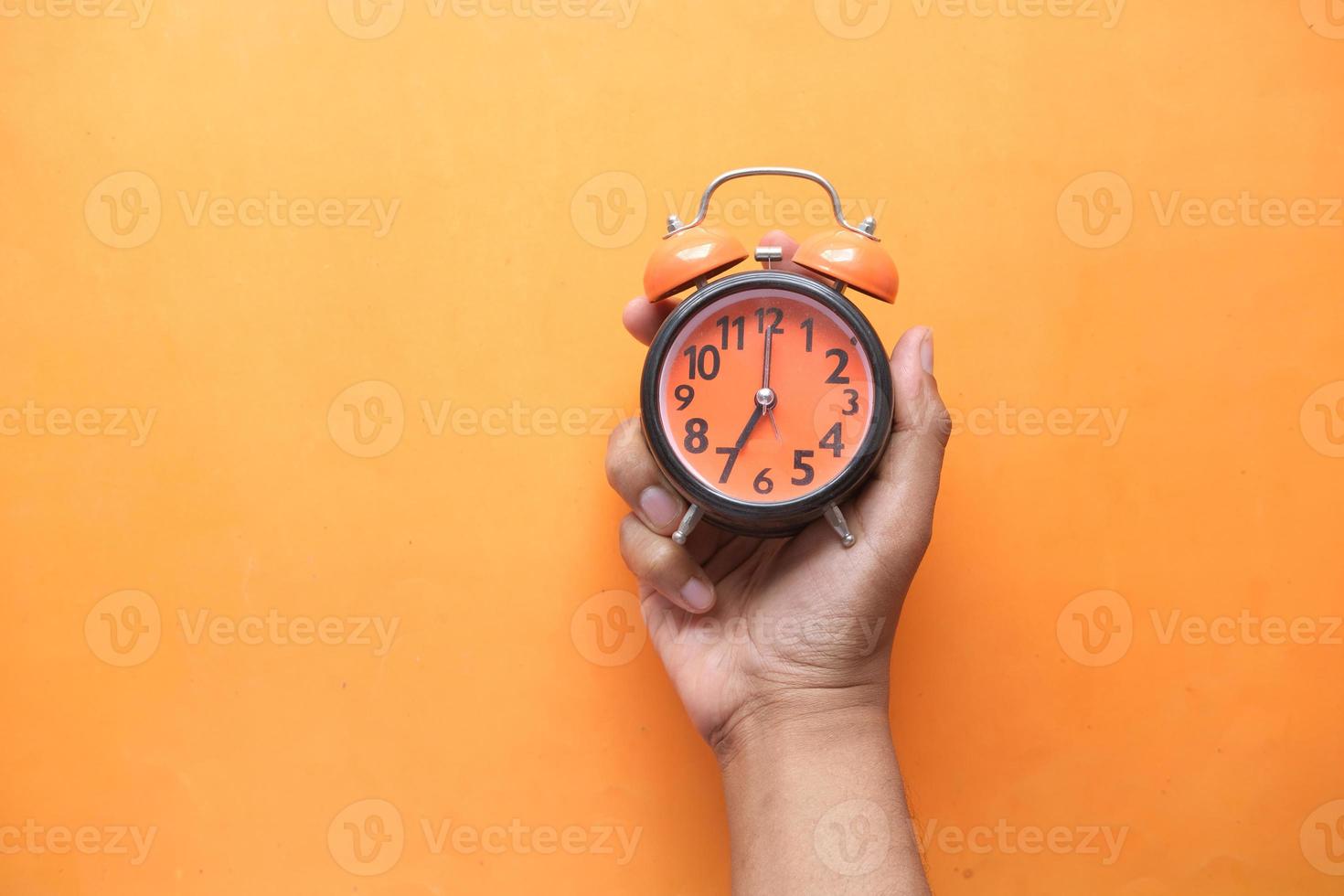 person hand holding alarm clock on orange background , photo
