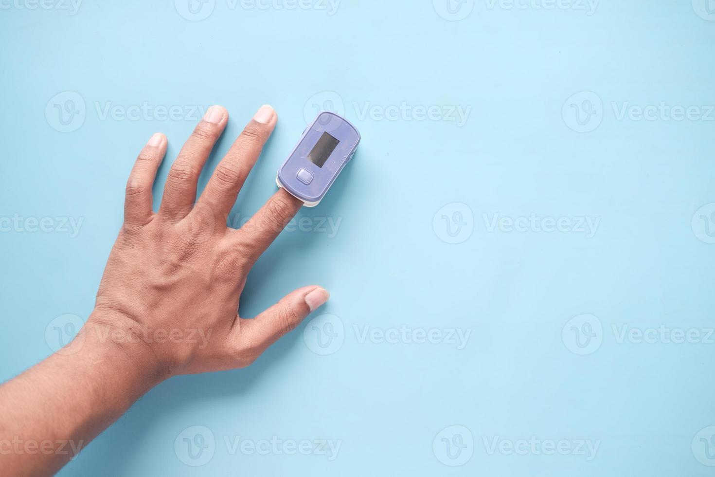 Cerca de la mano del hombre con oxímetro de pulso sobre fondo azul. foto