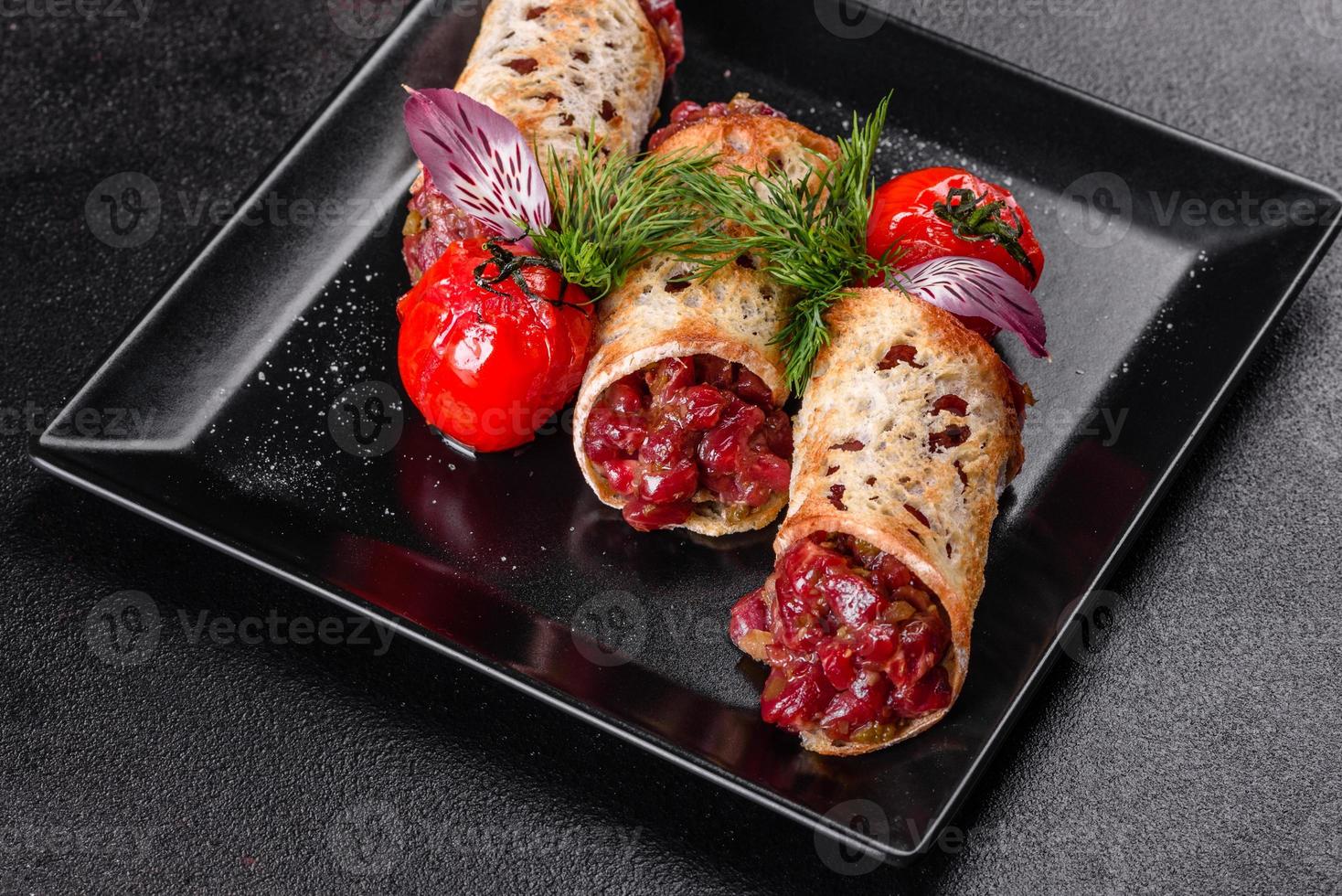 Delicioso tartar de ternera fresca con tostadas en una placa cuadrada negra foto