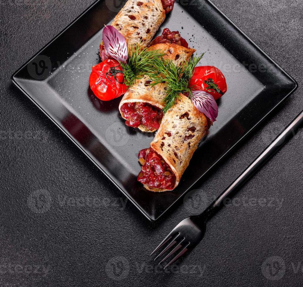 Delicious fresh beef tartar with toasts on a black square plate photo