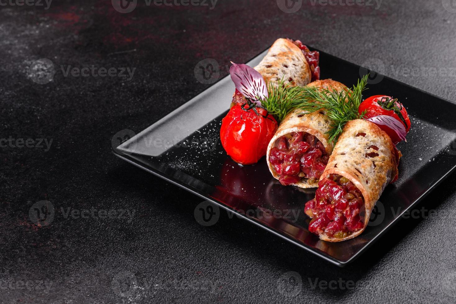 Delicious fresh beef tartar with toasts on a black square plate photo