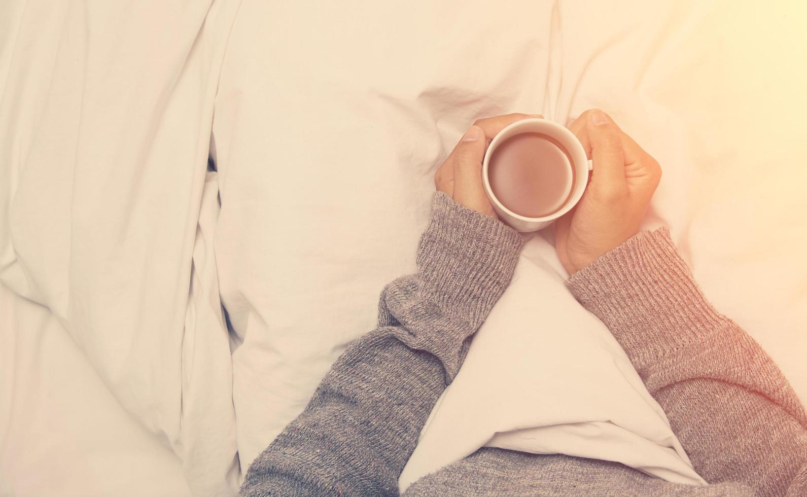 Hermosa joven bebiendo café en casa en la cama vistiendo un suéter foto