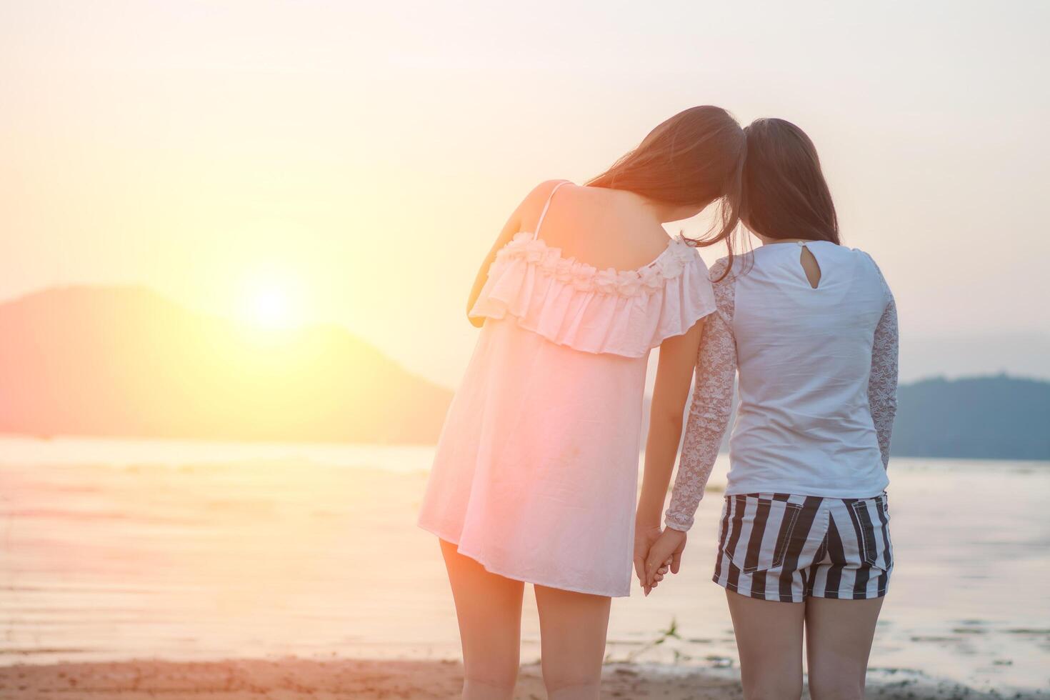 Two young women hold hands together on the beach looking at sunset photo