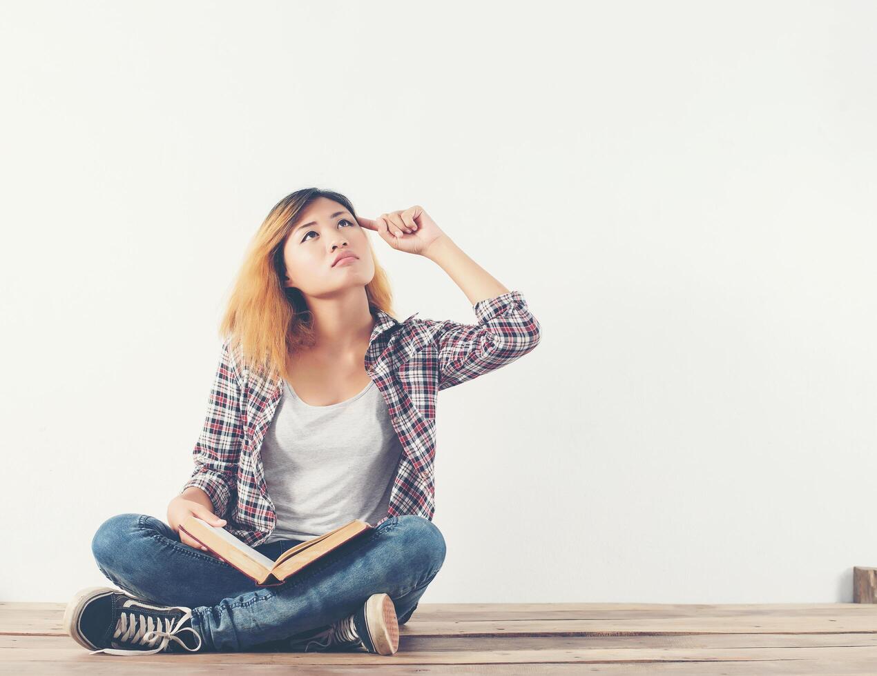 mujer joven inconformista sosteniendo libros y apuntando hacia arriba en aislados foto