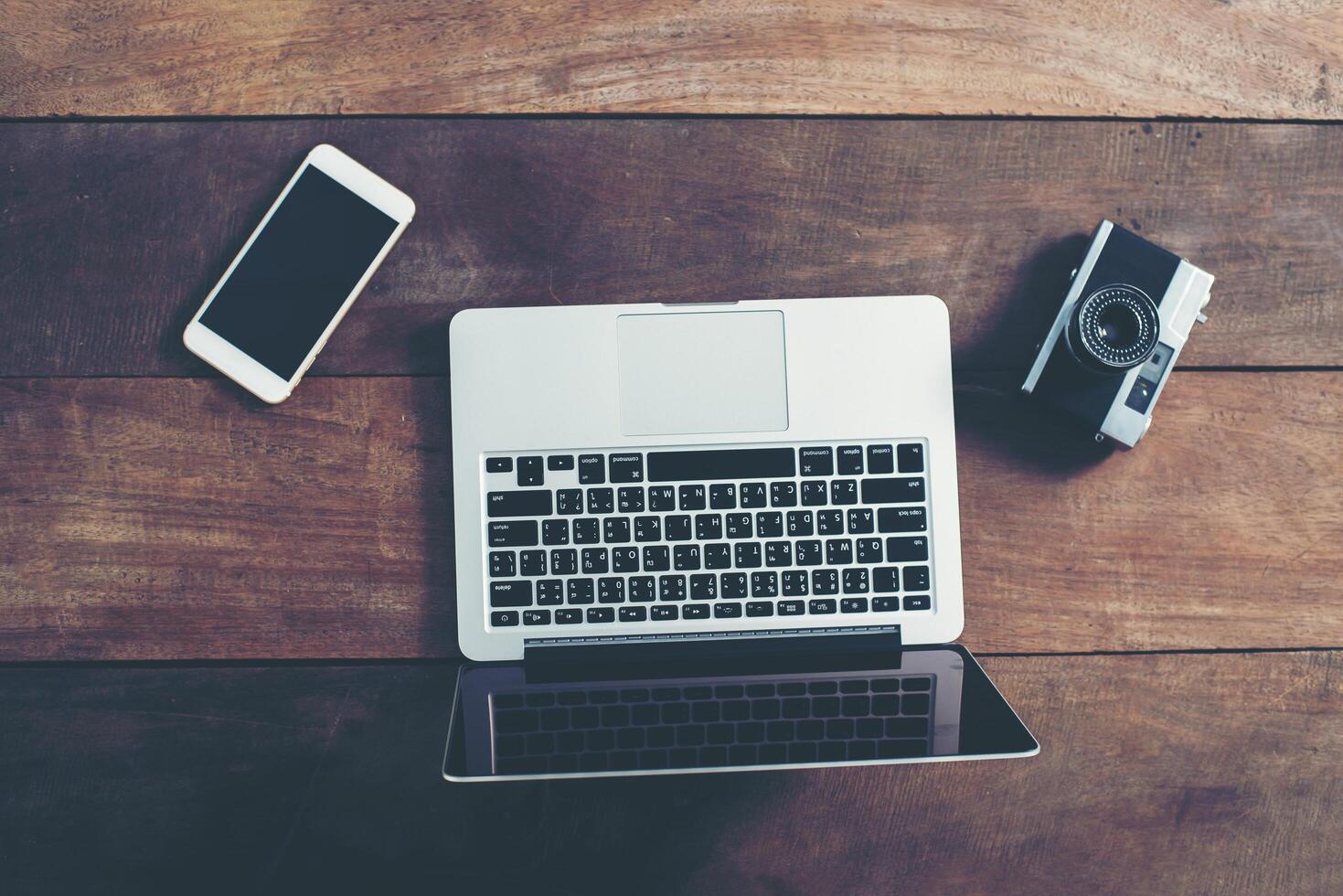 Top view of laptop, smartphone and retro camera on wooden table photo