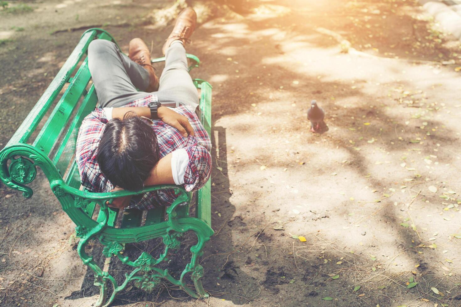 joven inconformista acostado en un banco del parque verde, mirando a otro lado. foto