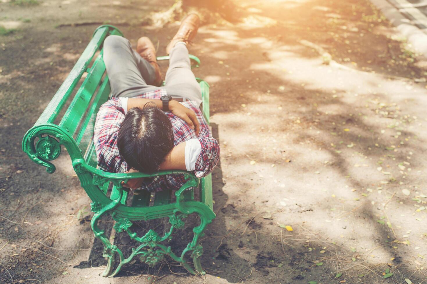 Young hipster man lying down on green park bench, looking away. photo