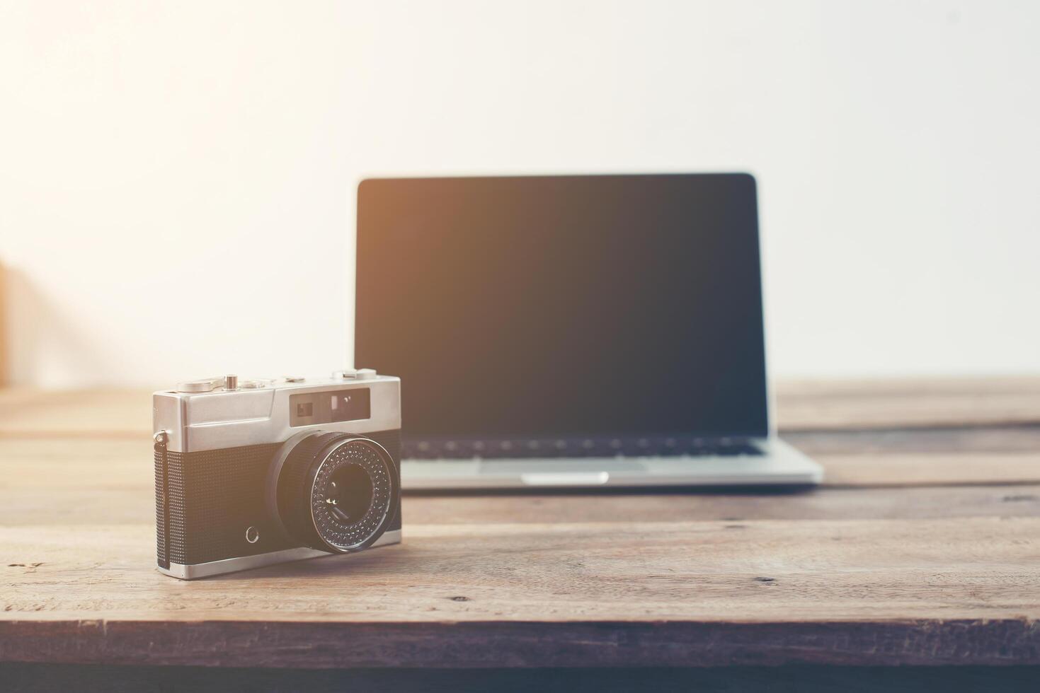 Laptop and retro camera on wooden table in retro tone photo