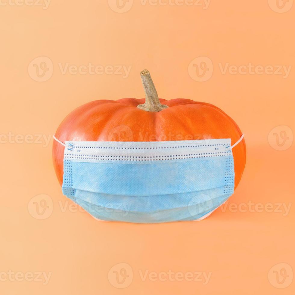 calabaza naranja en máscara médica sobre un fondo beige. foto