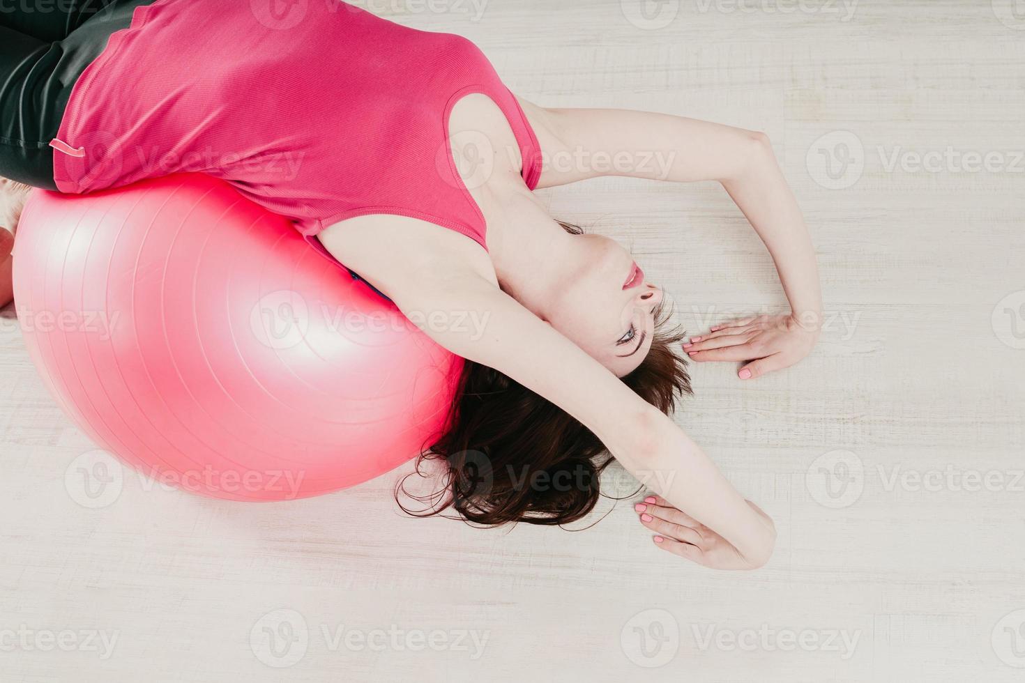 a girl making a bridge pose over a pink fitball in a gym photo