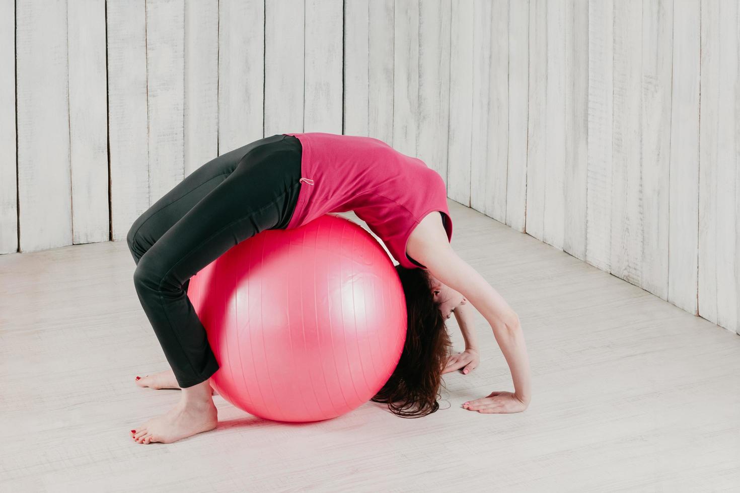 a girl making a bridge pose over a pink fitball in a gym photo