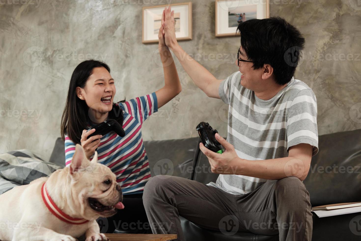 pareja asiática está jugando videojuegos y un perro mascota cerca. foto