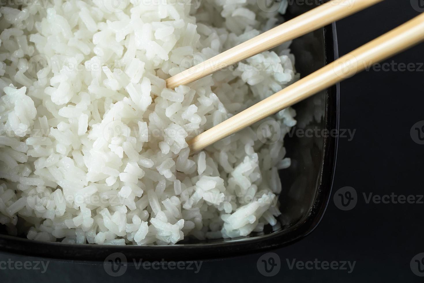 Bowl with boiled rice on black background. Asian food photo