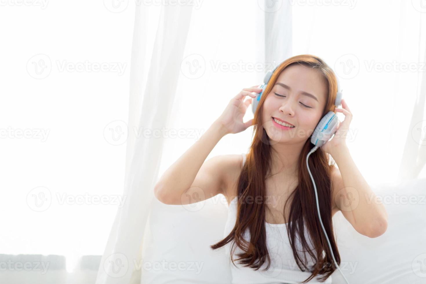 Joven mujer asiática disfruta de escuchar música con auriculares en el dormitorio foto