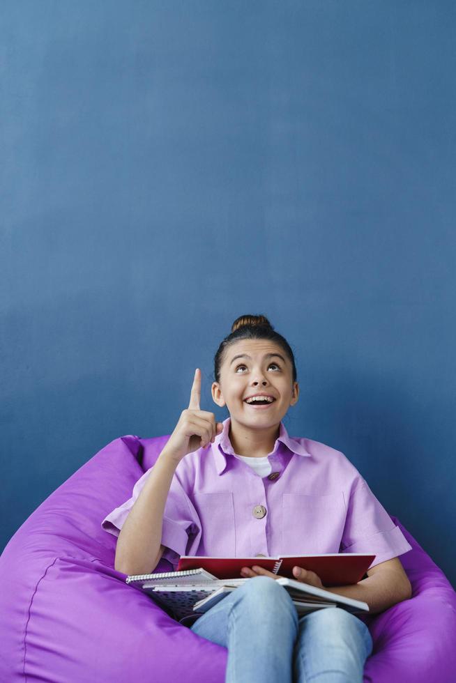 Teenage girl is sitting in a comfortable pouf, studying with a smile photo