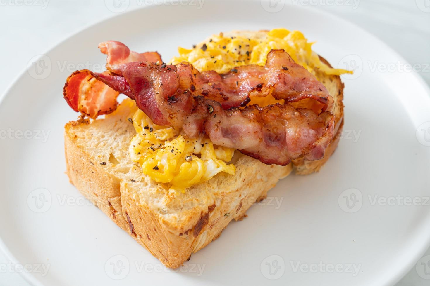 Tostadas de pan con huevos revueltos y tocino en la placa blanca. foto