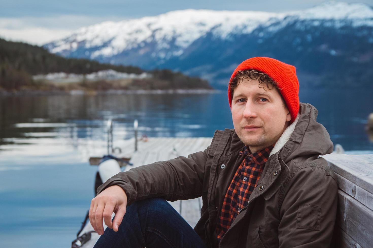 Portrait man sitting on wooden pier on the background of mountain photo