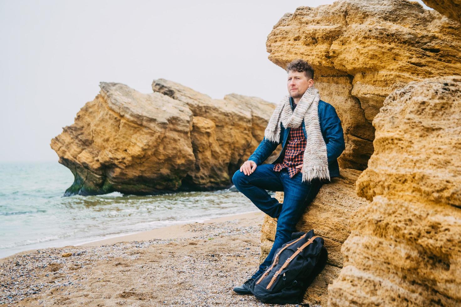 Man with a backpack standing near a rock against a beautiful sea photo