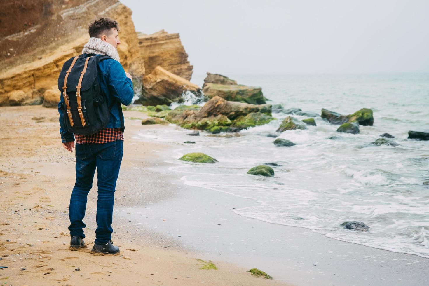 Hombre con una mochila de pie cerca de una roca frente a un hermoso mar foto