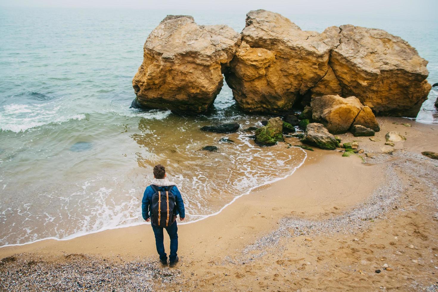 Man with a backpack standing near a rock against a beautiful sea photo