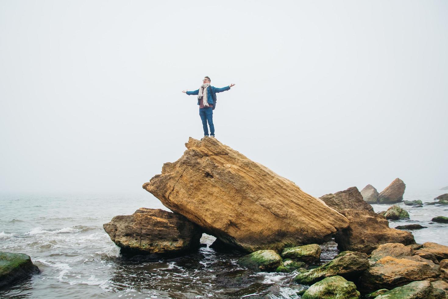 Hombre viajero con una mochila se encuentra en una roca frente a un hermoso mar foto