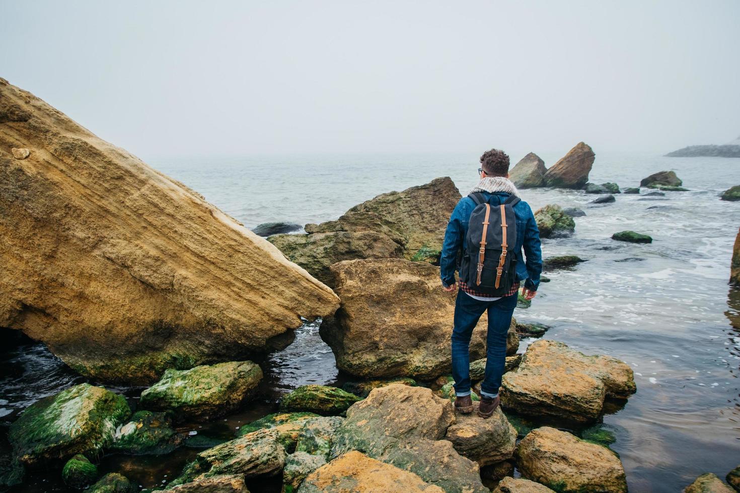 Traveler with a backpack stands on a rock against a beautiful sea photo