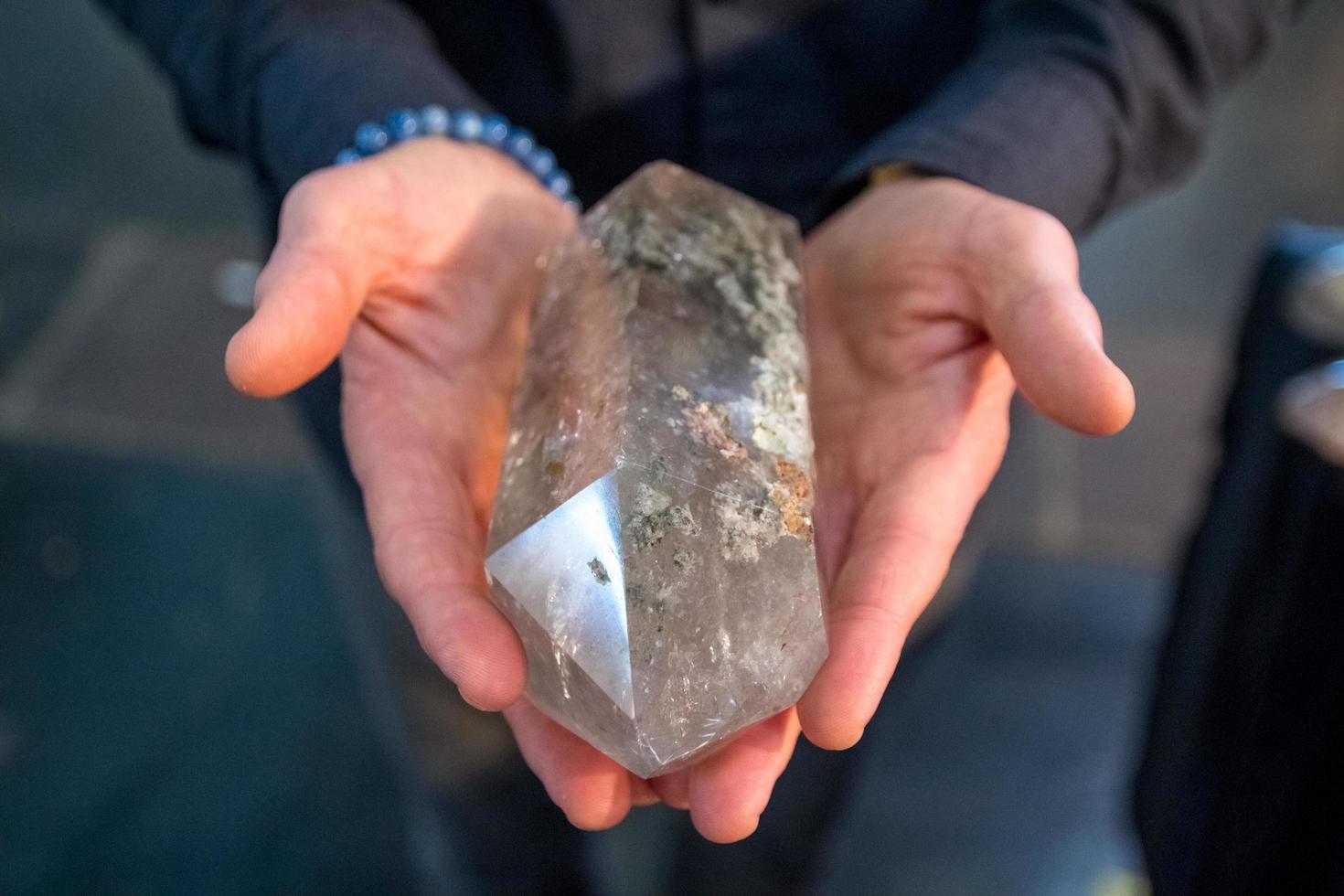 Las manos de un hombre que sostiene un gran cristal de cuarzo claro parecen poderosas. foto