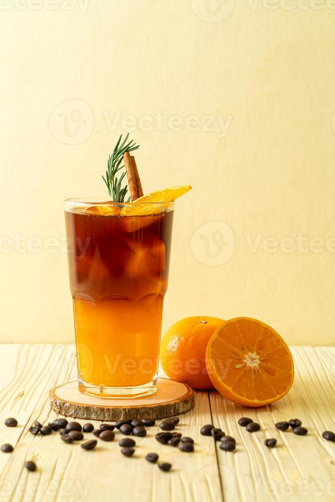 un vaso de café negro americano helado y una capa de jugo de naranja y limón decorado con romero y canela foto