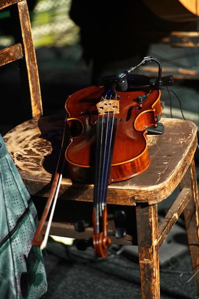 Primer plano de un violín con un arco en una silla de madera en la luz del sol foto