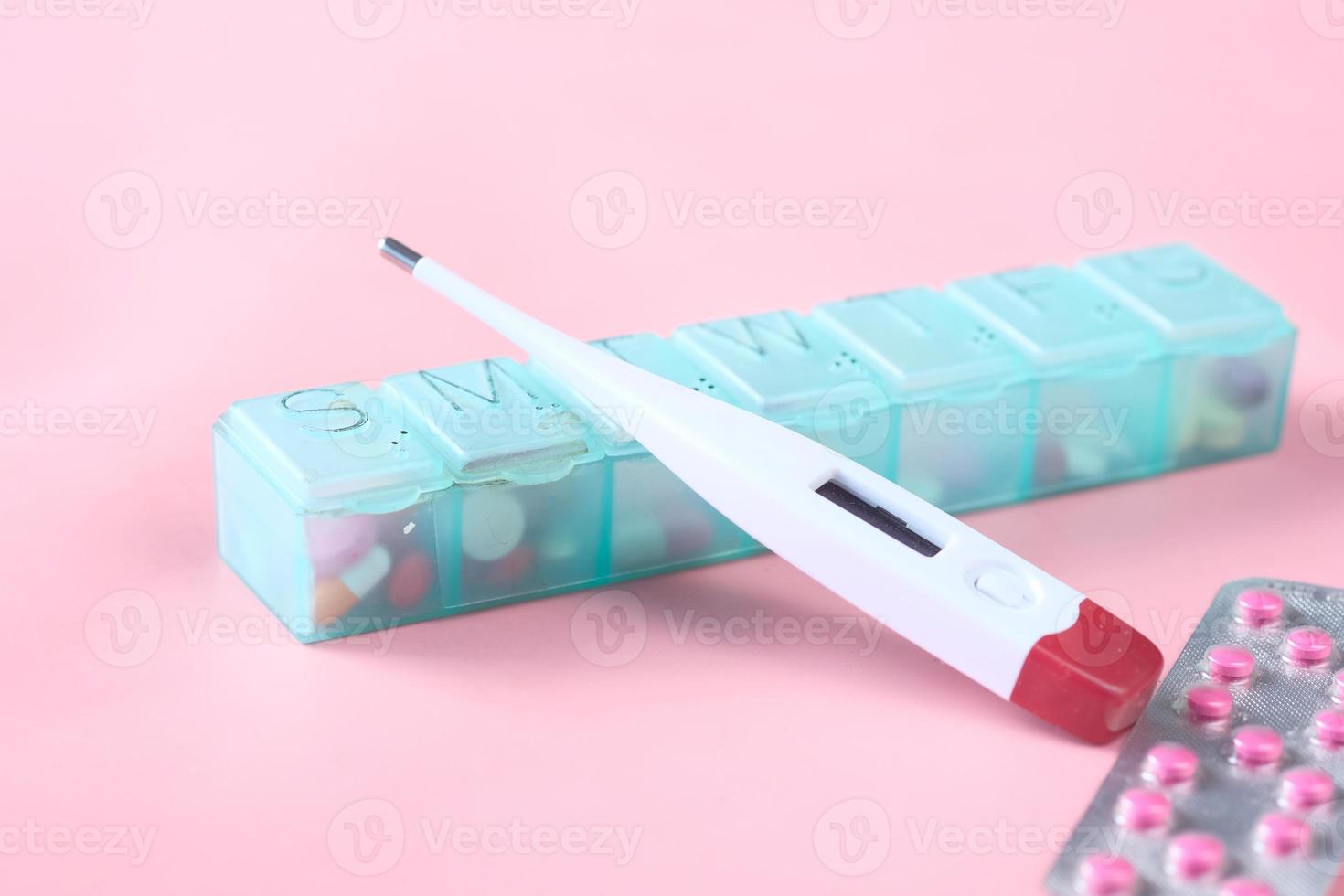 digital thermometer, pill container on a pink background photo