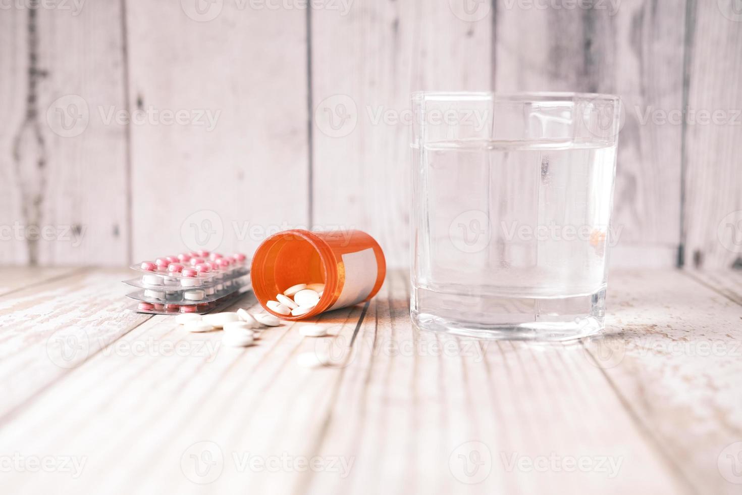 medical pill, blister pack and glass of water on table photo