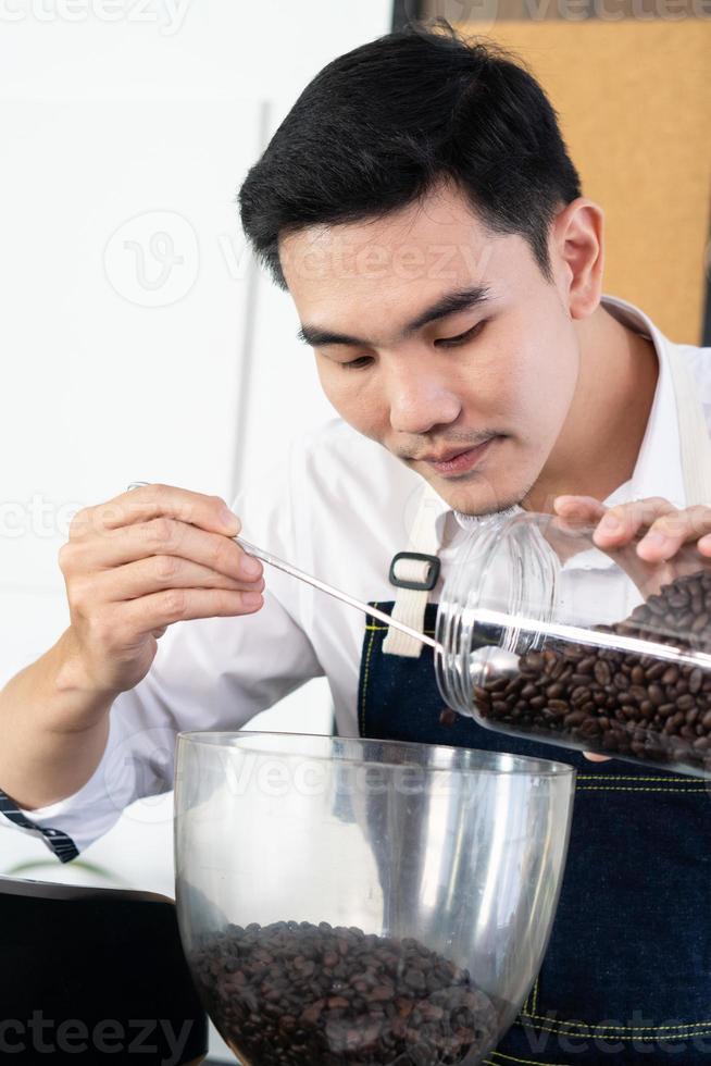young asian barista fills coffee beans into grinder machine in cafe photo