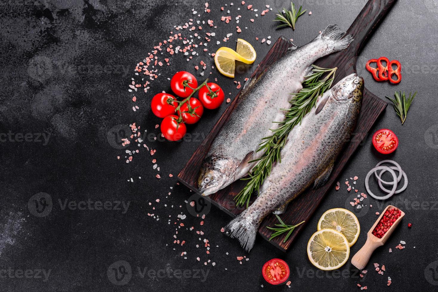 Raw trout lie on a black stone chopping board on a dark concrete table photo