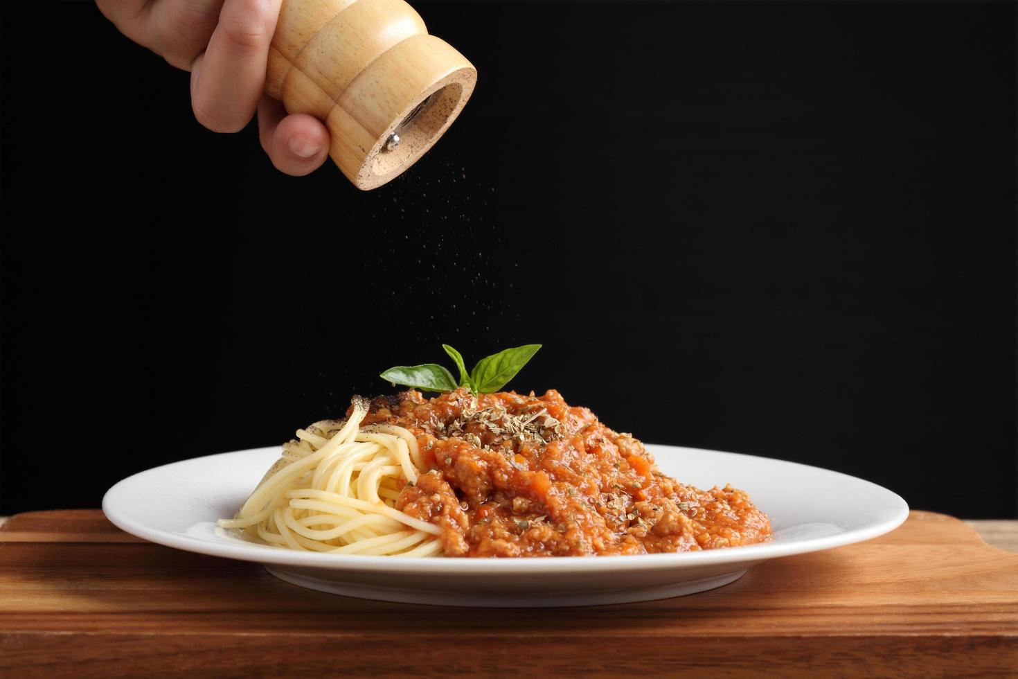 Mano sujetando el molinillo de pimienta con espaguetis y salsa roja en un plato blanco foto