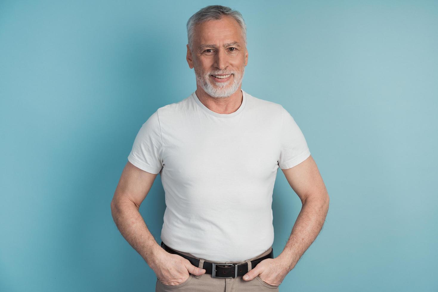 Senior, bearded man in a white T-shirt posing on a blue background photo