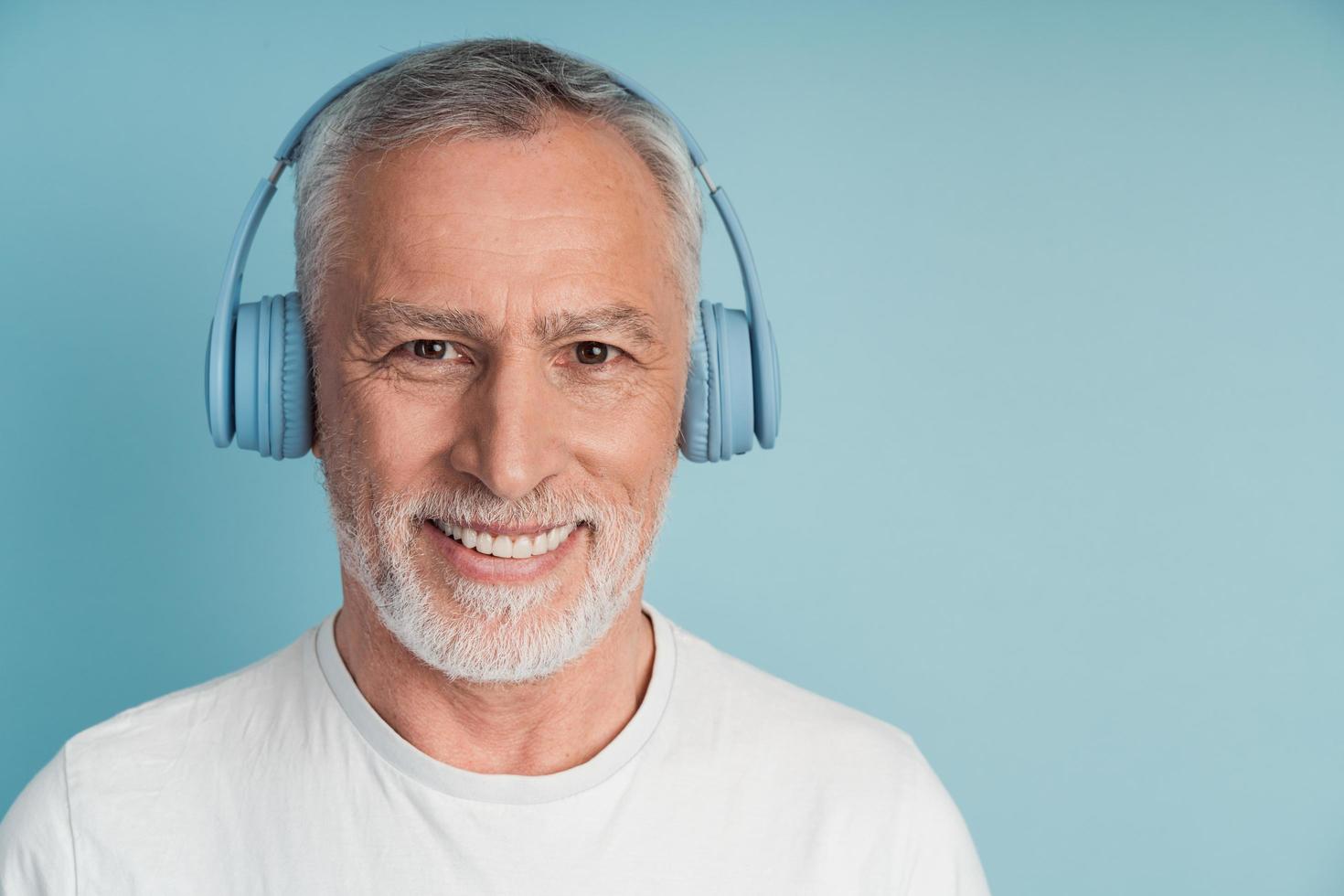 Vista cercana, hombre positivo en auriculares sonriendo sobre fondo azul. foto