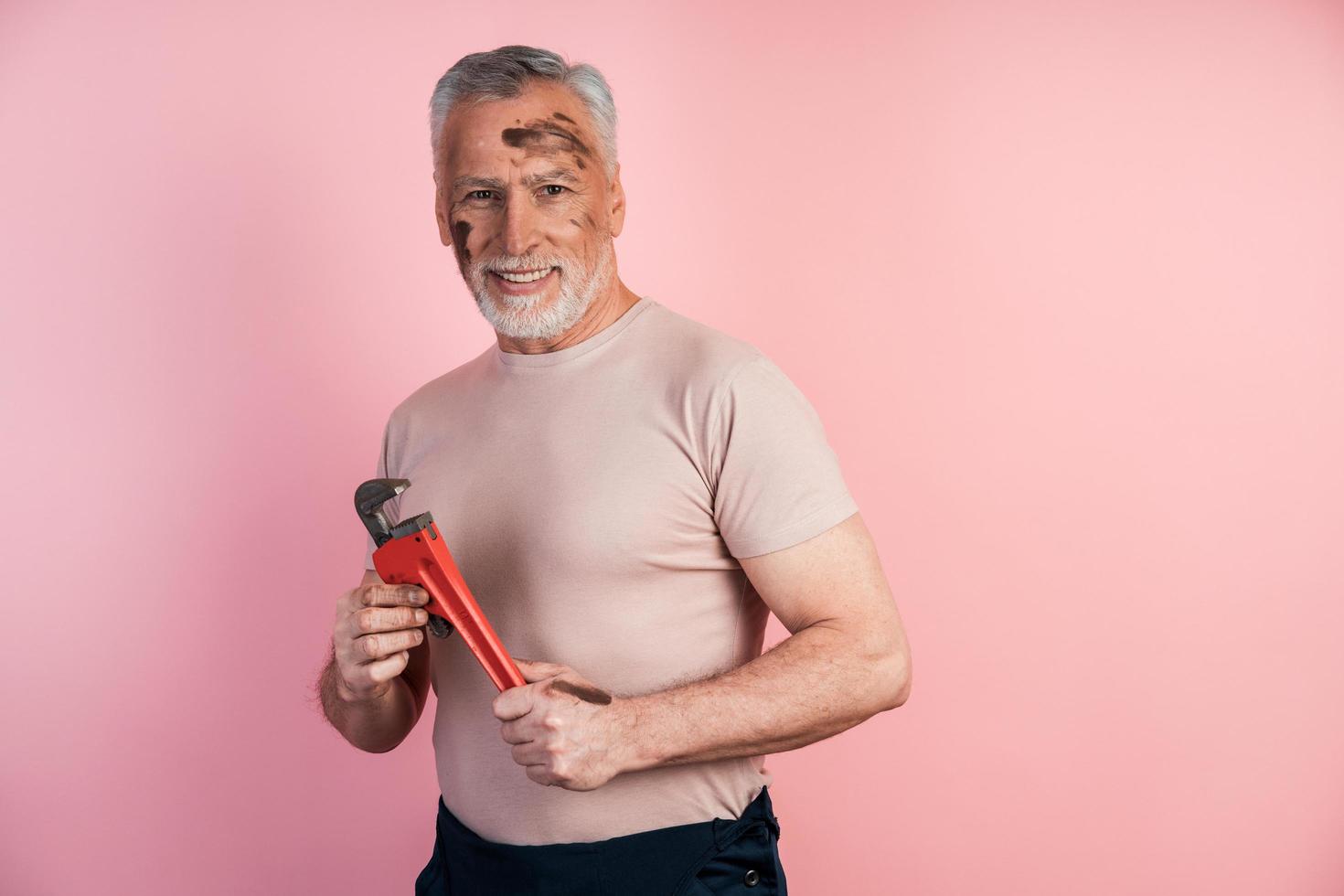 Gray-haired male builder smiles in his hand holding a wrench photo