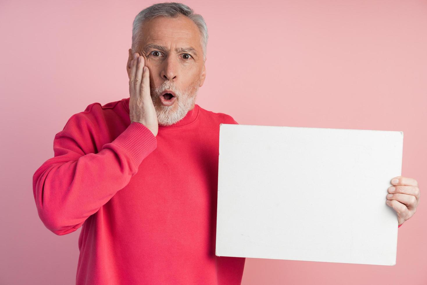 sorprendido hombre mayor que sostiene una hoja de papel en blanco. aislado foto