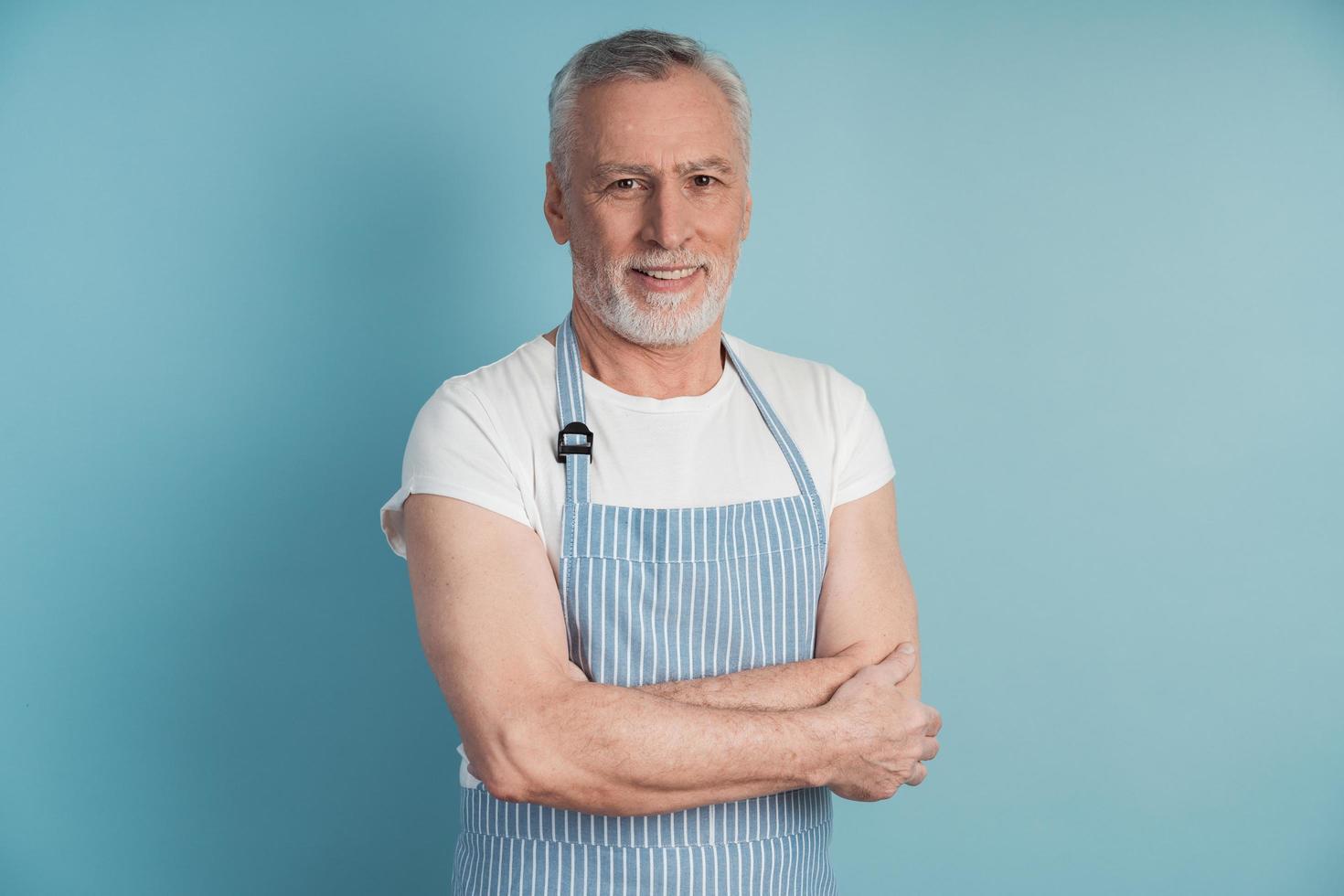 Attractive, elderly man in a blue apron posing on a blue background photo