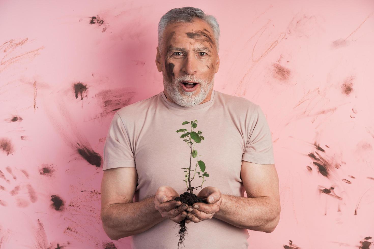 Amazed, senior man, gardener holding a plant for planting photo