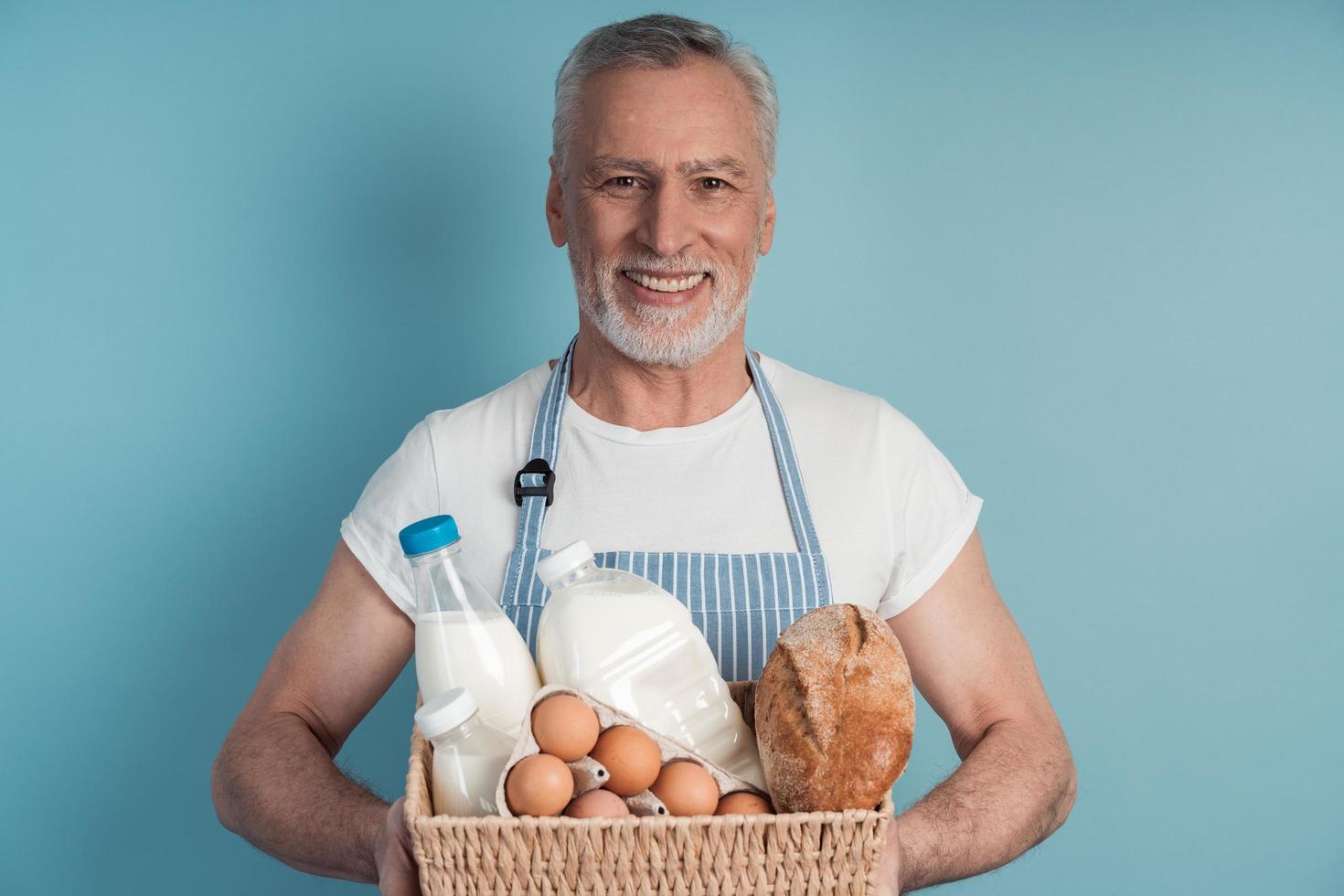 Un hombre mayor que sostiene una canasta con pan, leche, huevos foto