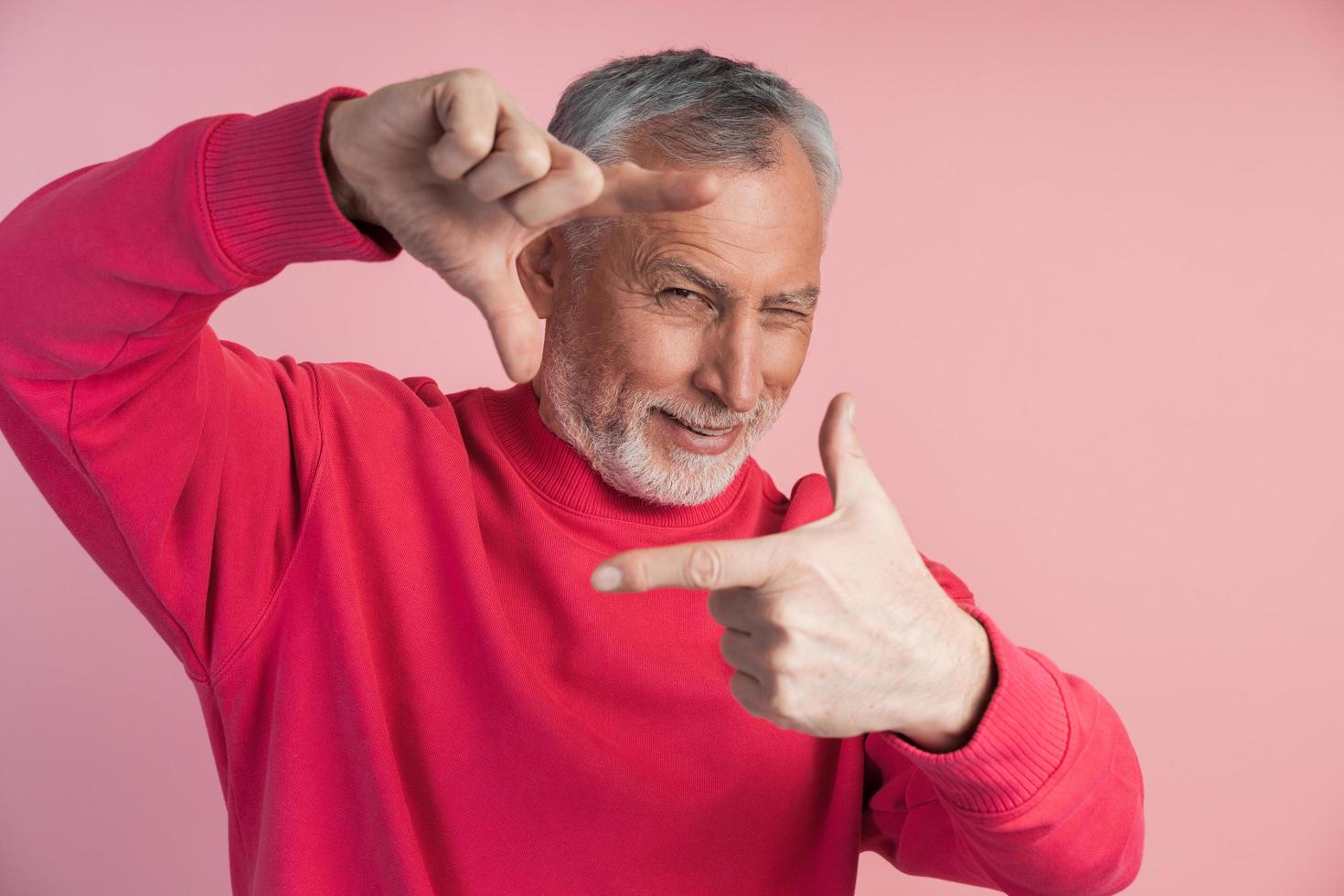 hombre de barba gris hace un marco con sus dedos, foto