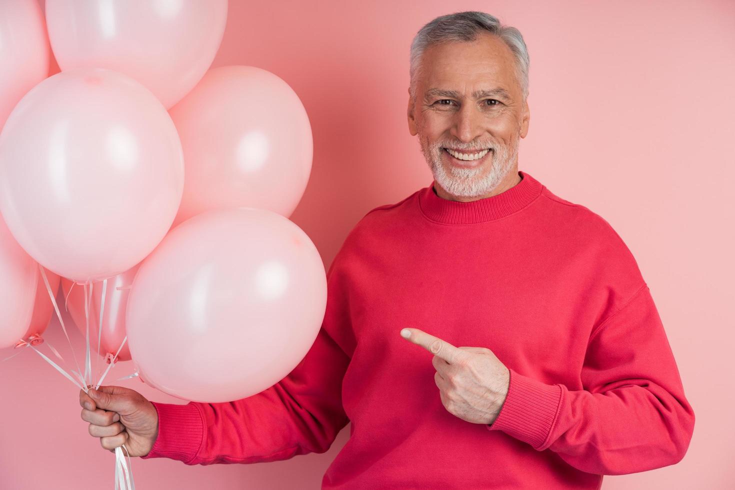 Smiling senior man holding balloons on a pink background photo