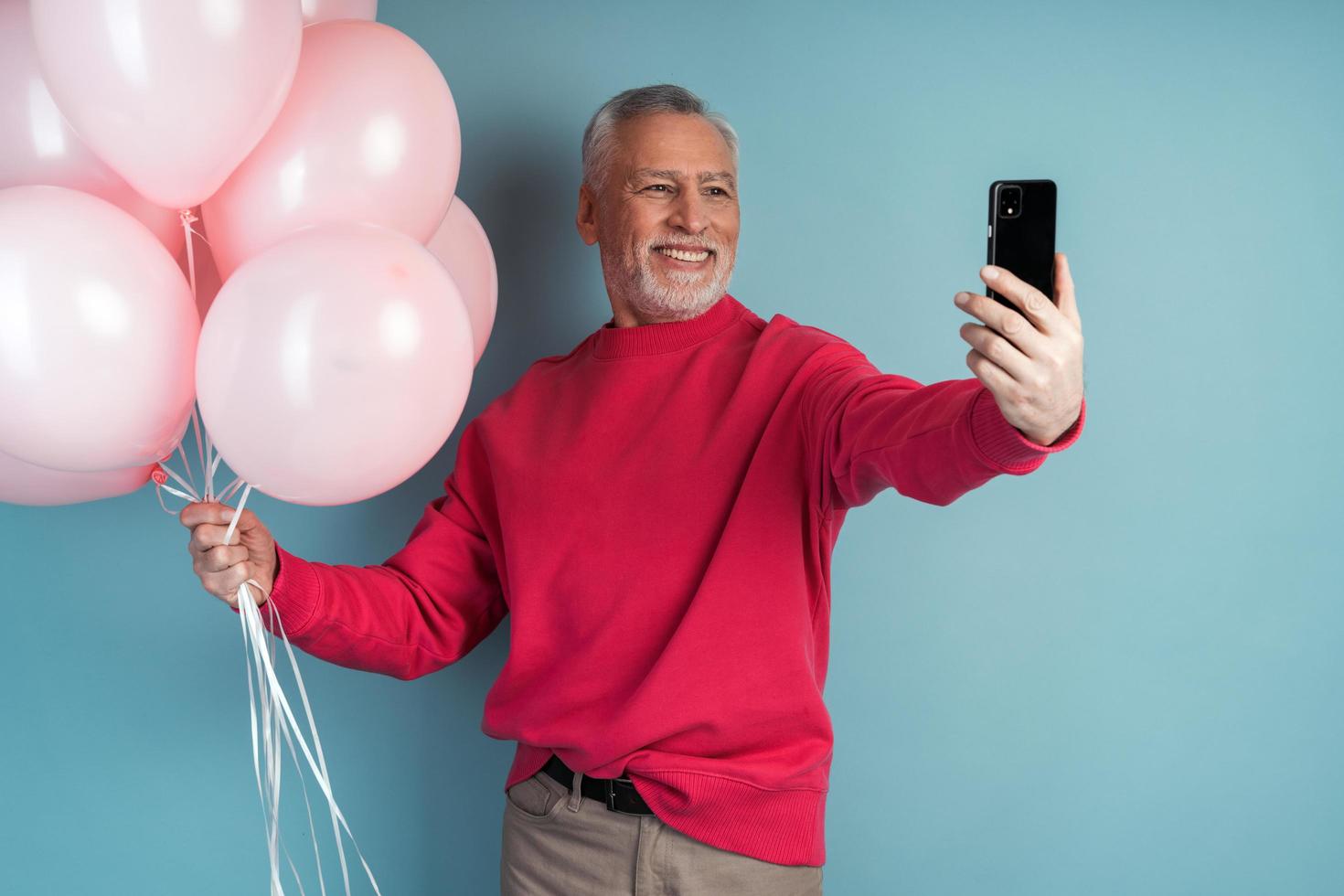 Attractive senior man holds balloons and takes a selfie photo