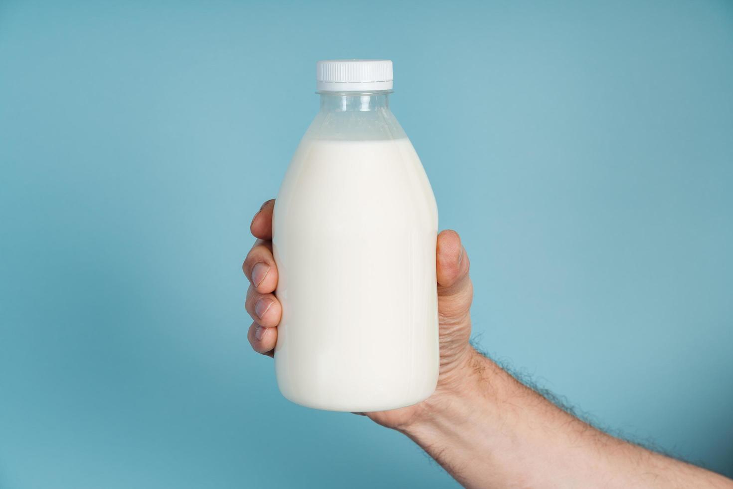 Mano masculina sostiene una botella de leche sobre un fondo azul. foto