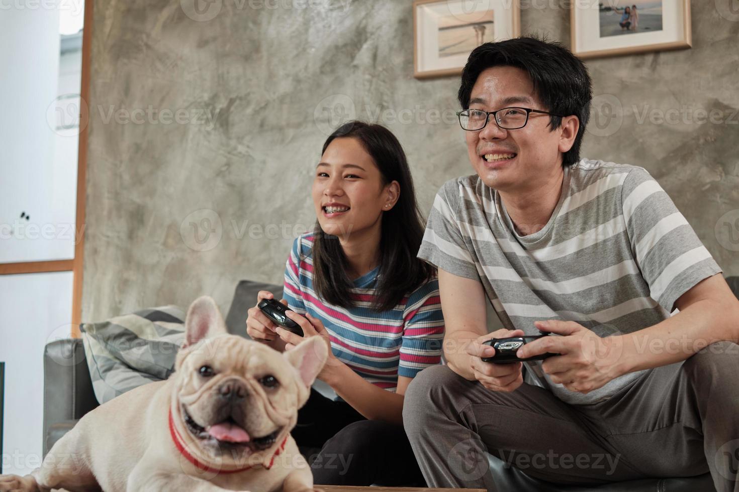 pareja asiática está jugando videojuegos y un perro mascota cerca. foto