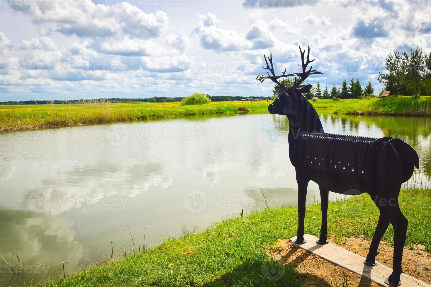 Unique hand metal deer grill standing in nature in front of lake photo